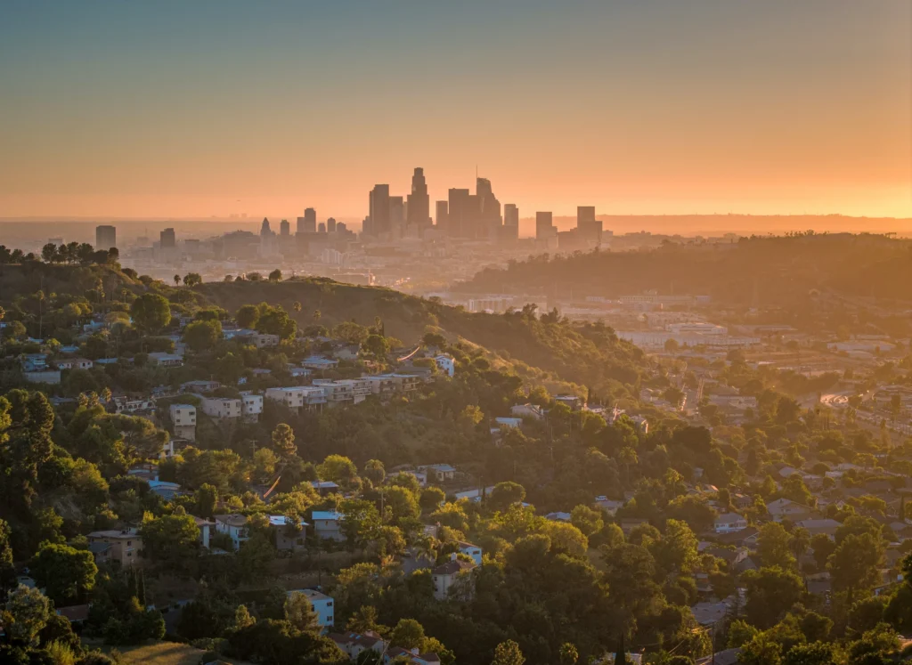 Silhouette de Los Angeles à l’horizon, au-delà de collines boisées au soleil couchant.